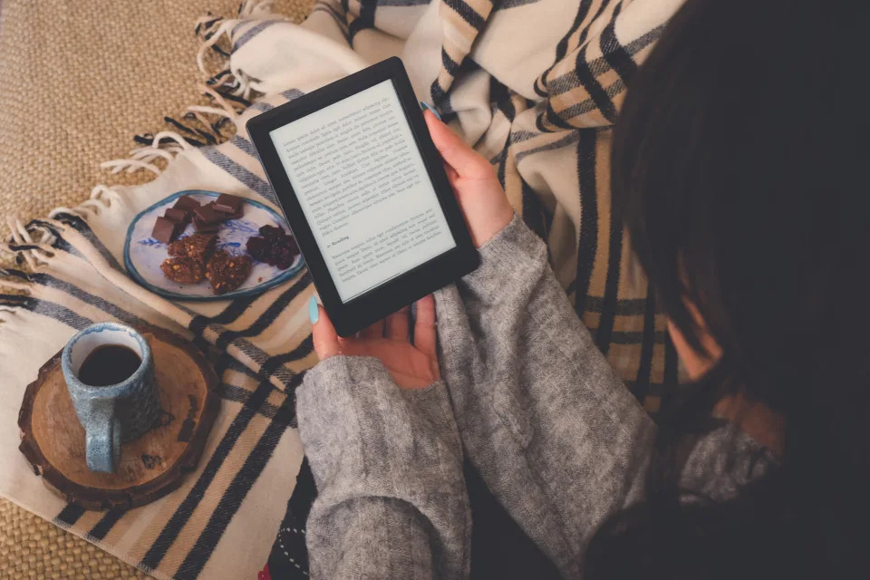 Top view of caucasian woman reading an e-book in the e-book reader with a cup of coffee and cocoa cookies. Cozy winter day at home and hygge concept. The text on the e-book reader is an 