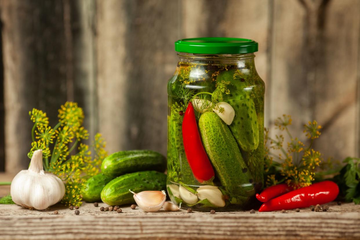 Pickled cucumbers in glass jars and spices and vegetables for preparation of pickles on wooden background.