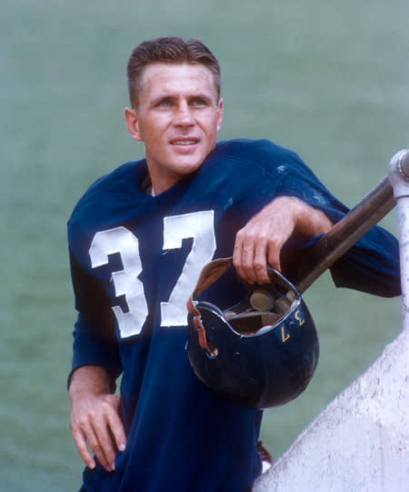 Doak Walker leans against a railing while holding his helmet.