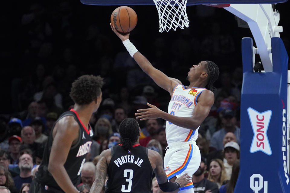 Oklahoma City Thunder guard Shai Gilgeous-Alexander, right, shoots in front of Houston Rockets forward Jae'Sean Tate, left, and guard Kevin Porter Jr. (3) during the first half of an NBA basketball game Wednesday, Dec. 1, 2021, in Oklahoma City. (AP Photo/Sue Ogrocki)