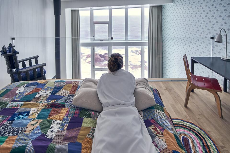 A woman in a bath robe laying on her bed in her Fogo Island Inn suite