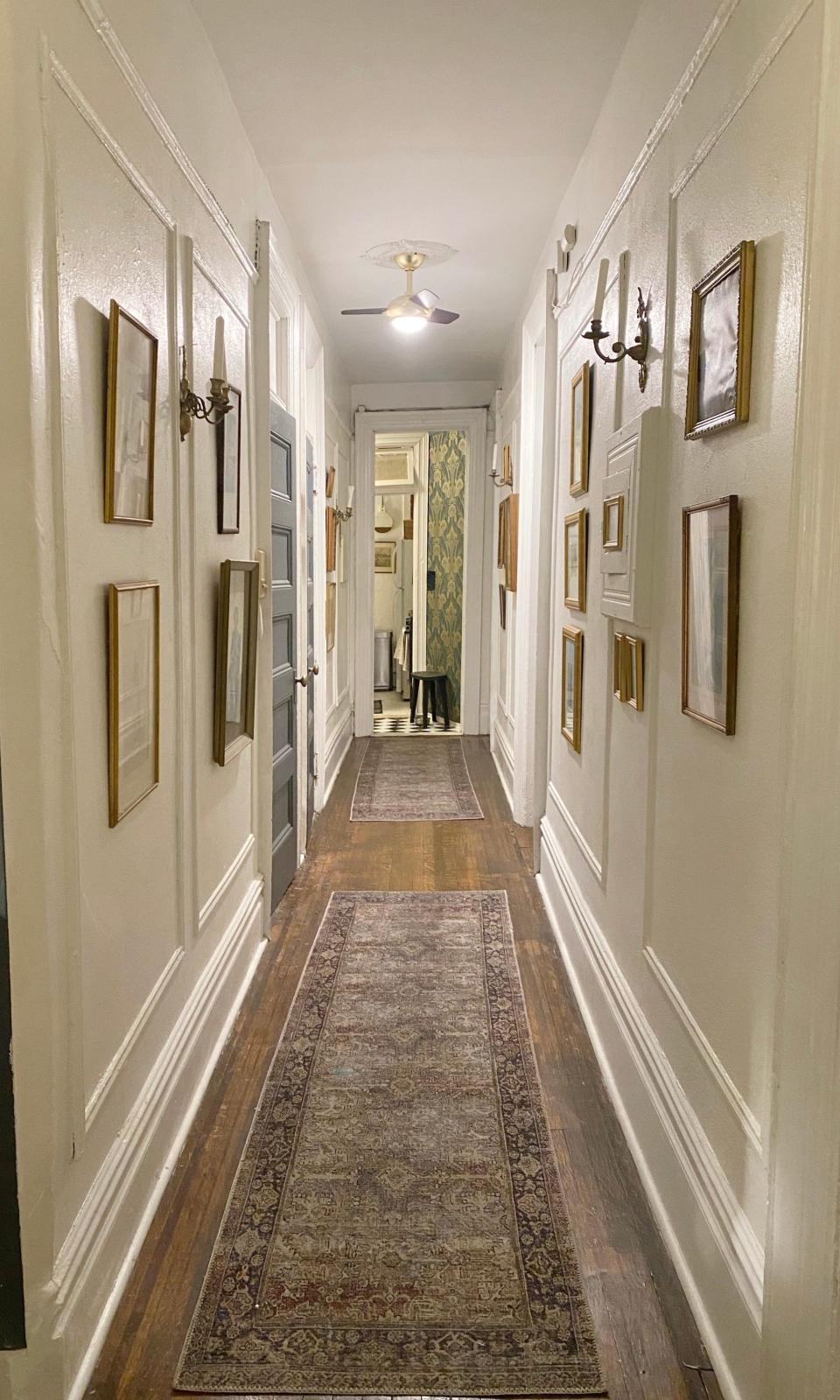 A hallway with white walls covered in framed artwork with runners on the floor.