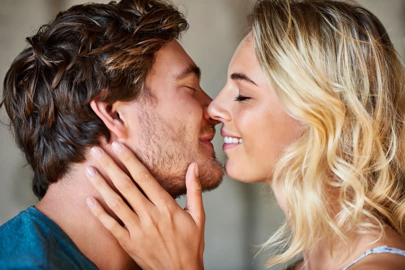 Close-up side view of young couple kissing. Romantic male and female partners spending quality time together. They are at home.