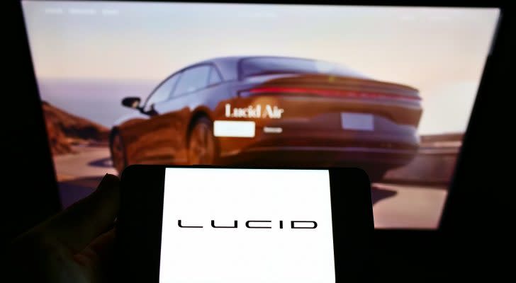 Someone is viewing a red Lucid (LCID) Air car on a computer screen while holding a phone that says Lucid