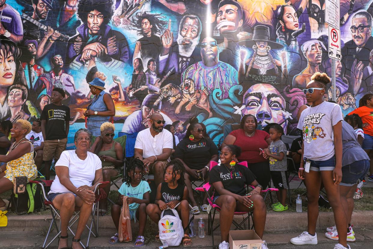 Families sit on a curb on Chicon street in front of a mural of influential black icons during the annual Juneteenth parade in East Austin on June 19, 2022.