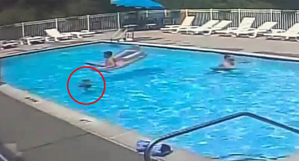 A drowning child can be seen under the surface of an apartment complex swimming pool, as an adult on an inflatable drifts over the top of them, seemingly unaware.