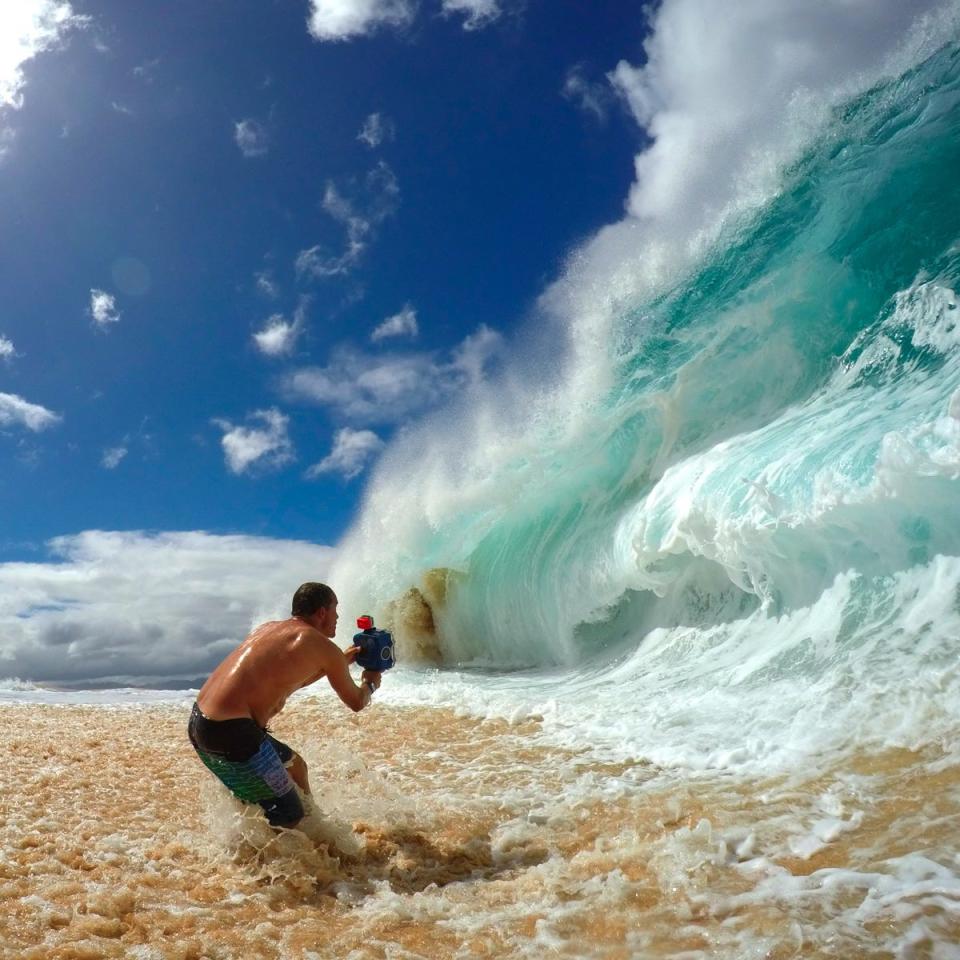 Clark standing in shallow water capturing a powerful shorebreak wave on the North Shore of Oahu.
