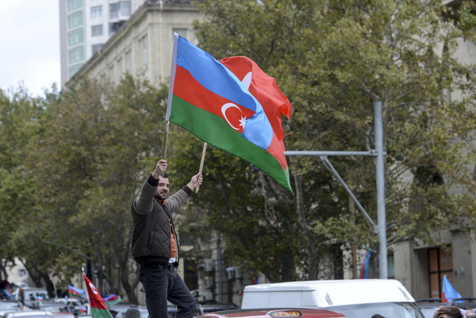 An Azerbaijani man with the national flag celebrates after the country's President claimed Azerbaijani forces have taken Shushi, a key city in the Nagorno-Karabakh region that has been under the control of ethnic Armenians for decades in Baku, Azerbaijan, Sunday, Nov. 8, 2020. (AP Photo)
