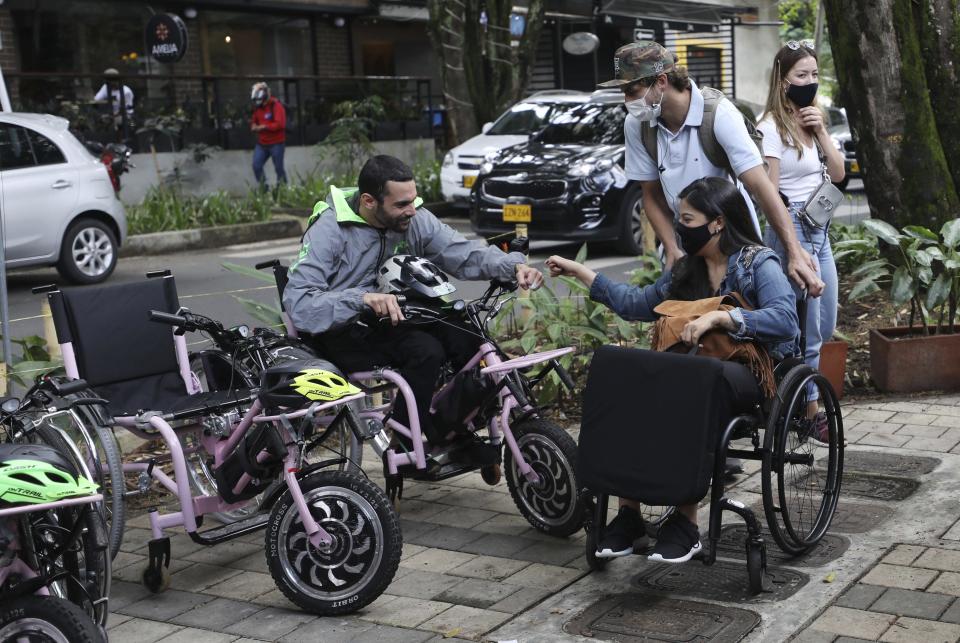 Martin Londoño, left, owner of MATT, an electric wheelchair tour company, greets a client in Medellin, Colombia, Wednesday, Nov. 18, 2020. Londoño, an entrepreneur who lost the use of his legs in a traffic accident is organizing electric wheelchair tours for people with disabilities or fully abled folks, in a bid to generate employment for people while creating awareness of the challenges faced by those on wheelchairs. (AP Photo/Fernando Vergara)