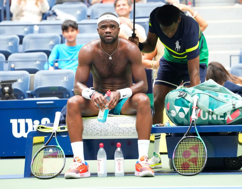 Frances Tiafoe sits shirtless on his player bench mid-match.