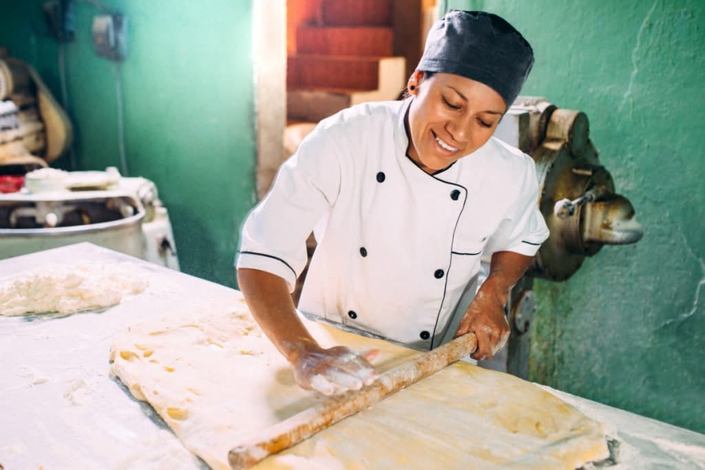 A woman rolls out dough as she prepares to bakes pastries. 