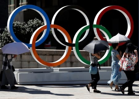 Passersby holding sunshades walk past Olympic rings displayed at Nihonbashi district in Tokyo