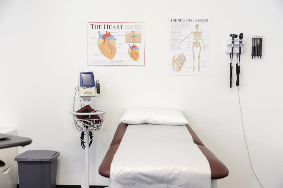 Doctor's office exam room with a medical bed, diagnostic tools on the wall, and posters of the heart and skeletal system