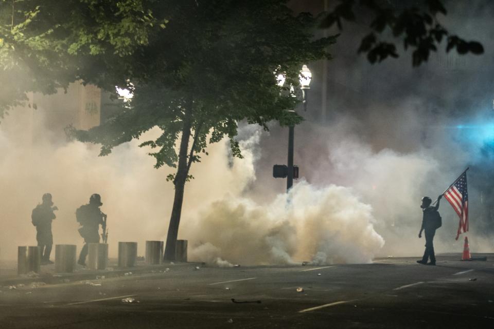 Federal officers and a protester carrying an American flag face off.