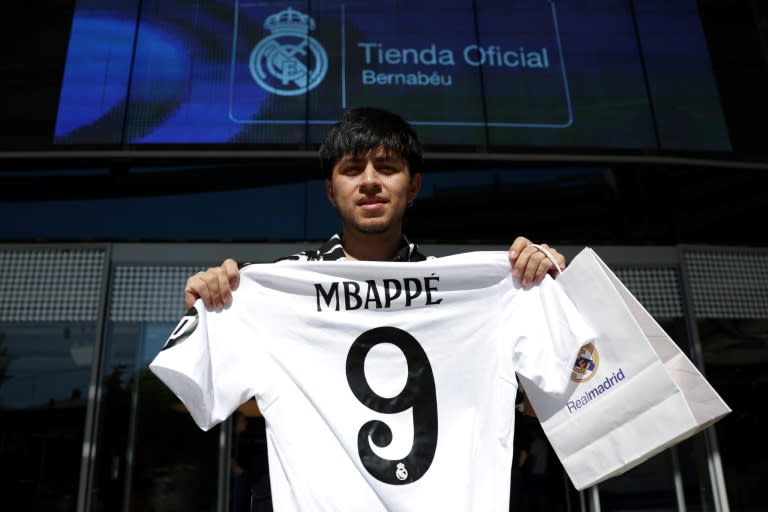 Un supporteur pose avec un maillot du Real floqué Kylian Mbappé, devant une boutique du club, le 11 juillet 2024 à Madrid (Pierre-Philippe MARCOU)