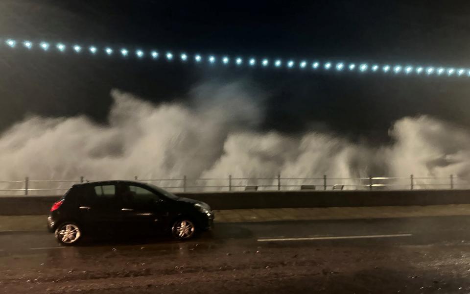 A vehicle passes by as the breeze of high waves caused by storm Ciaran is seen in the background, in Penzance,