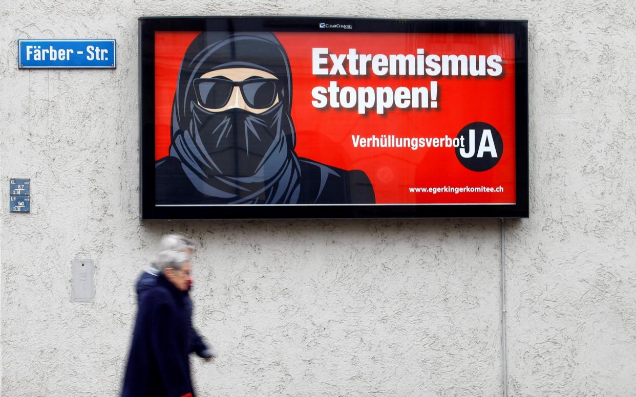Pedestrians walk past a campaign poster promoting a 'burka ban'. The poster shows an image of a woman with her face covered alongside the words "Stop extremism! Veil ban - Yes" - REUTERS/Arnd Wiegmann