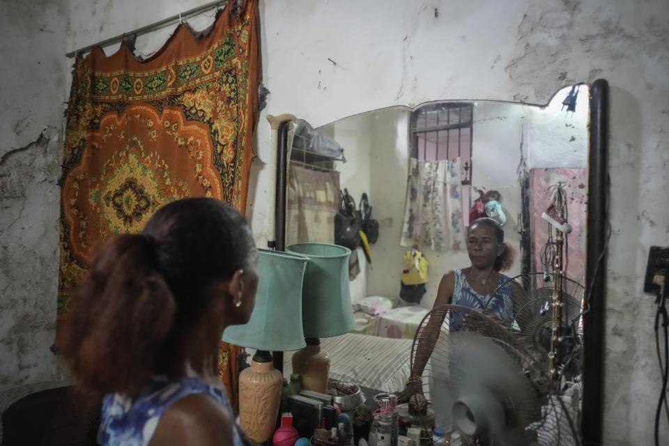 Maricelys Colás poses for a portrait in the mirror of her bedroom inside the dilapidated mansion where she lives with five other families on Villegas Street in Havana, Cuba, Thursday, Oct. 5, 2023. “How can we not live in fear? Every time it rains I feel like small pebbles come falling down on me,” said the retired 64-year-old who has lived in the house with her 85-year-old mother for 59 years. (AP Photo/Ramon Espinosa)