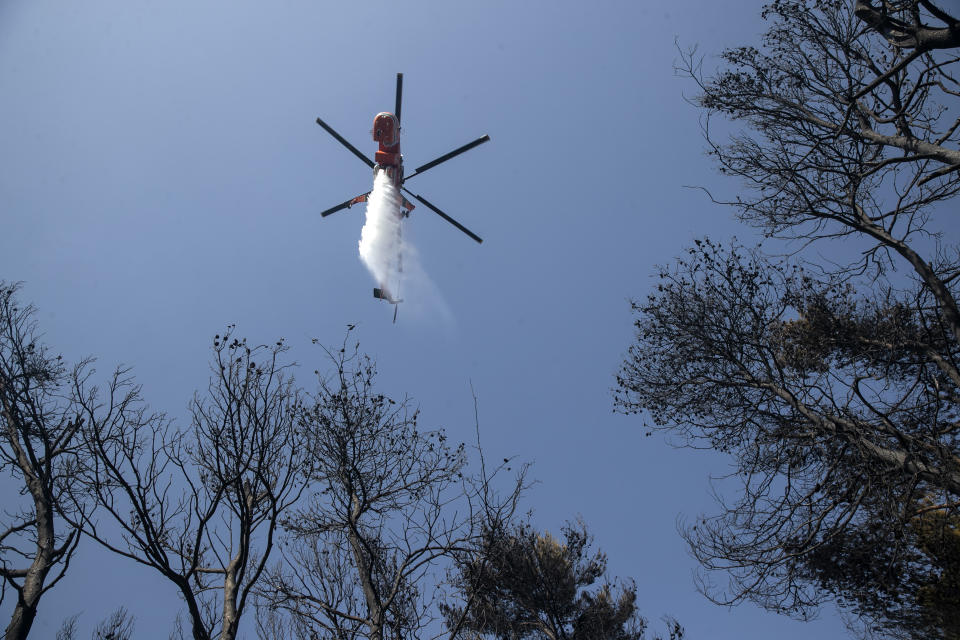 A firefighting helicopter drops water during a forest fire at Dionysos northern suburb of Athens, on Tuesday, July 27, 2021. Greek authorities have evacuated several areas north of Athens as a wildfire swept through a hillside forest and threatened homes despite a large operation mounted by firefighters. (AP Photo/Yorgos Karahalis)