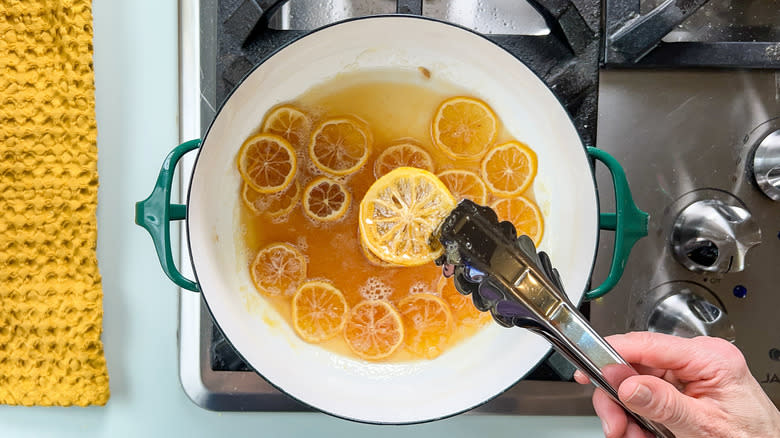 Candied lemon wheels in syrup in saucepan on stovetop with tongs