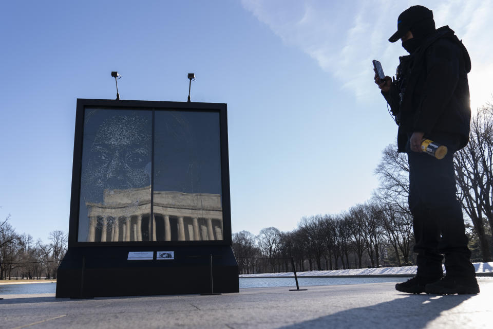 A security guard photographs the installation "Vice President Kamala Harris Glass Ceiling Breaker" at the Lincoln Memorial, reflected, in Washington, Wednesday, Feb. 4, 2021. Vice President Kamala Harris' barrier-breaking career has been memorialized in a portrait depicting her face emerging from the cracks in a massive sheet of glass. Using a photo of Harris that taken by photographer Celeste Sloman, artist Simon Berger lightly hammered on the slab of laminated glass to create the portrait of Harris. (AP Photo/Carolyn Kaster)