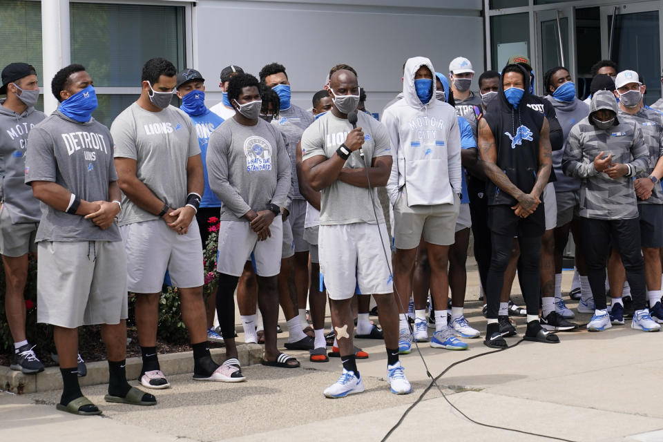 Duron Harmon speaks into a microphone surrounded by his teammates. They are all wearing face coverings.