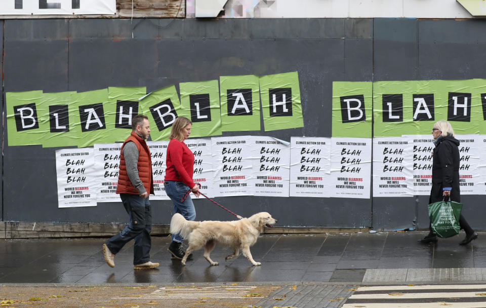 People walk past posters placed by climate activists ahead of a protest march by them through the streets of Glasgow, Scotland, Friday, Nov. 5, 2021 which is the host city of the COP26 U.N. Climate Summit. The protest was taking place as leaders and activists from around the world were gathering in Scotland's biggest city for the U.N. climate summit, to lay out their vision for addressing the common challenge of global warming. (AP Photo/Scott Heppell)