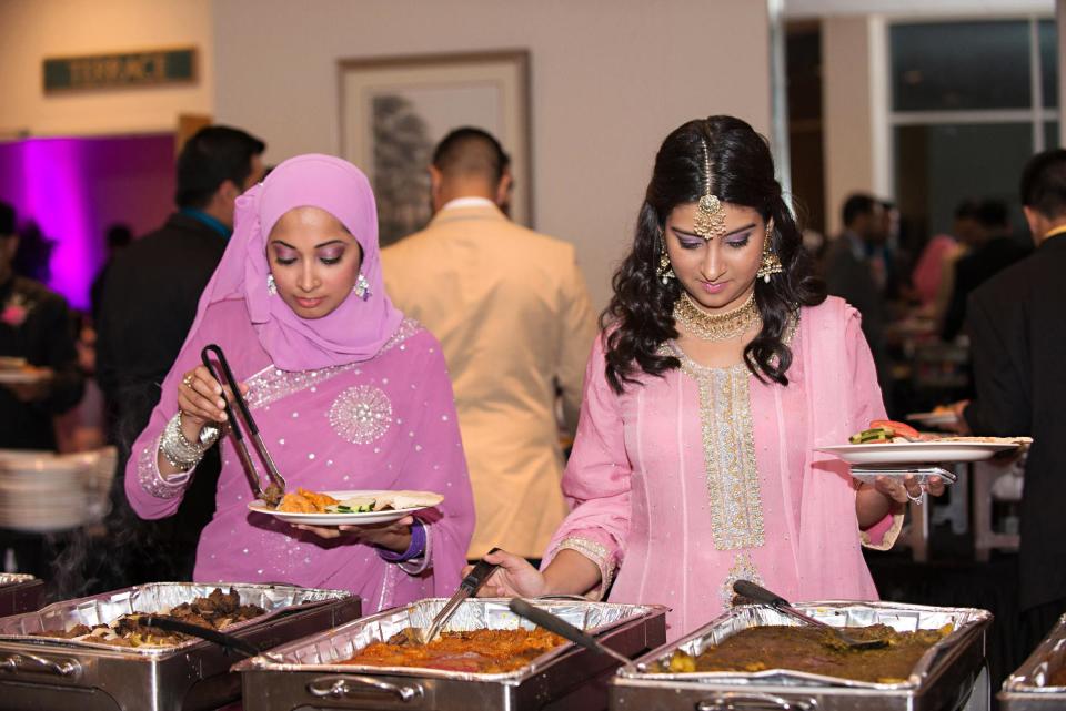 This July 2013 photo provided by Lynn Barsigian Photography shows the wedding guests of Ateeb Ansari and Sheema Aleem serving themselves some of the Indian food that an outside caterer prepared for the event at Owego Treadway Inn & Conference Center in New York. The groom’s family wanted a venue that allowed outside catering for the reception so they could serve a meal that met their religious and cultural needs. (AP Photo/Lynn Barsigian Photography)
