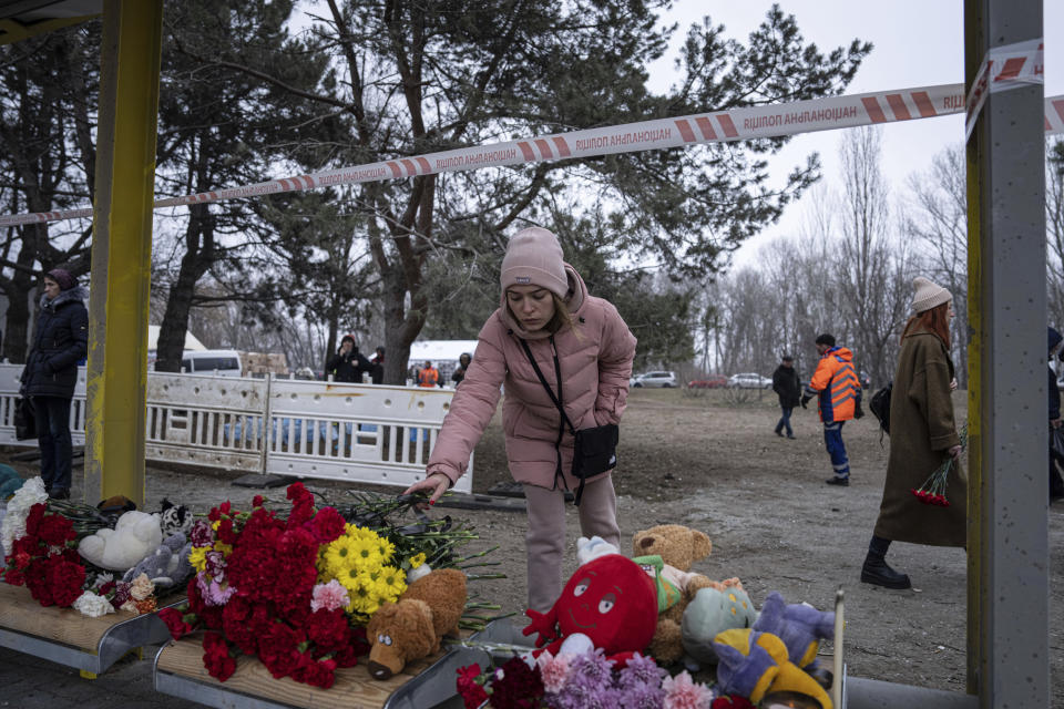 A woman lays flowers at a bus stop, for people who were killed in a Russian missile strike on an apartment building in the southeastern city of Dnipro, Ukraine, Monday, Jan. 16, 2023. (AP Photo/Evgeniy Maloletka)
