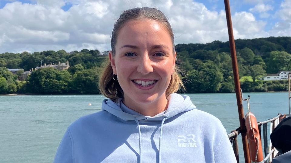 Anna Hume smiling at the camera, in front of the waters of the Menai Strait