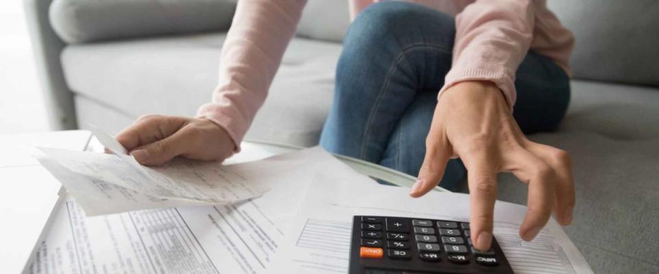 Close up of woman sitting on couch, using calculator on top of pile of papers