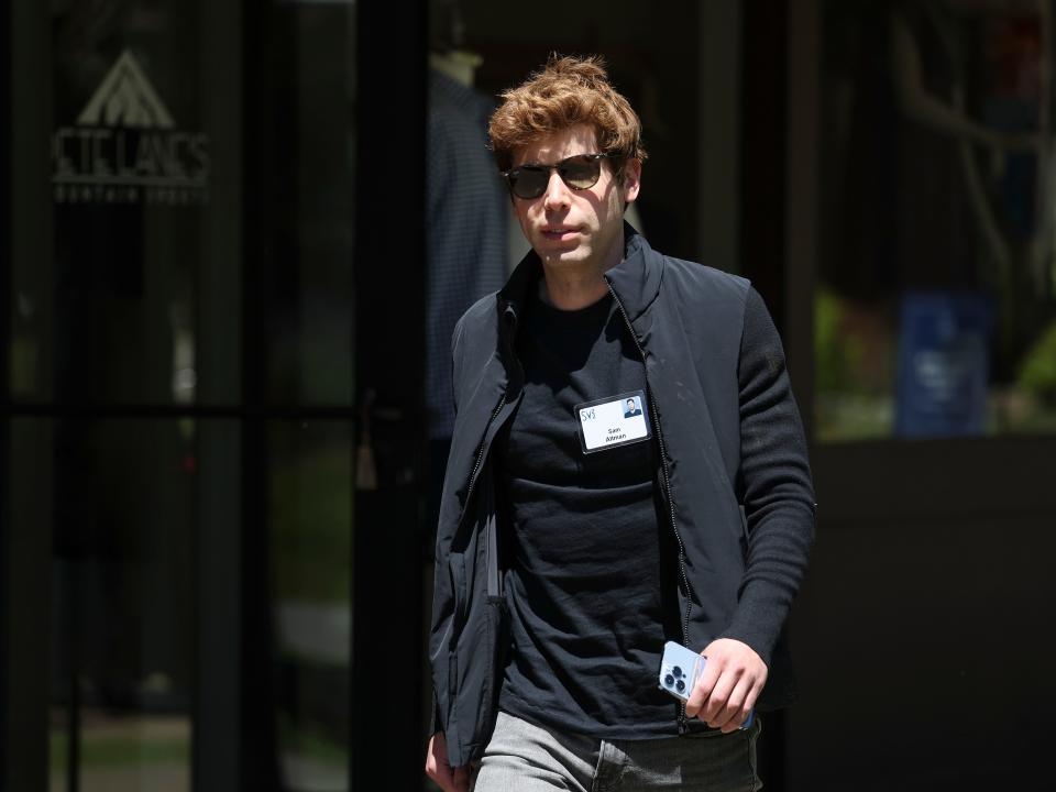 sam altman wearing a black t shirt, black jacket, grey pants and sunglasses