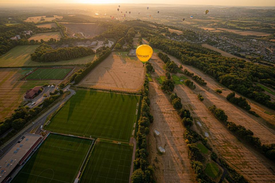 A hot air balloon flies over a browning and parched golf course (Ben Birchall/PA) (PA Wire)