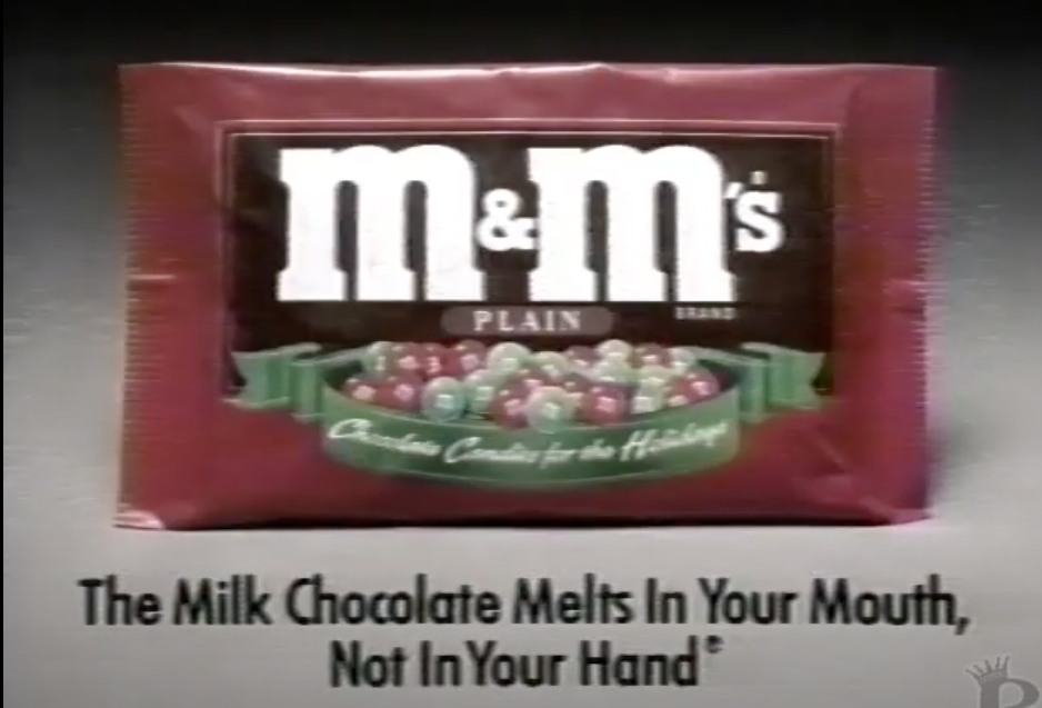 Screenshot from M&M's commercial, with a bag of the holiday M&M's and text, "The Milk Chocolate Melts in Your Mouth, Not in Your Hand"