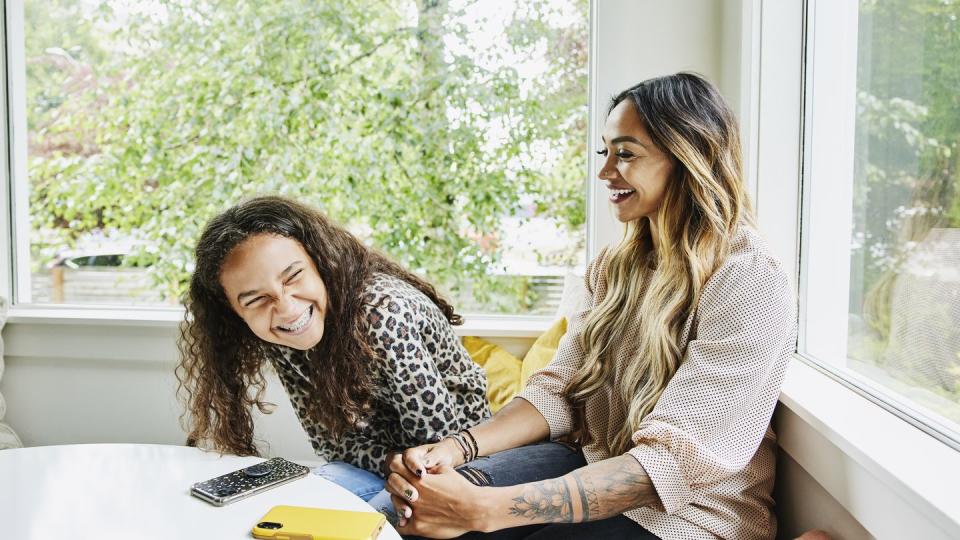 medium shot of mother and daughter laughing together while hanging out in living room