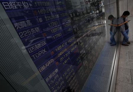 A pedestrian looks at his mobile phone stands in front of an electronic board showing various stock prices outside a brokerage in Tokyo, Japan, September 4, 2015. REUTERS/Yuya Shino