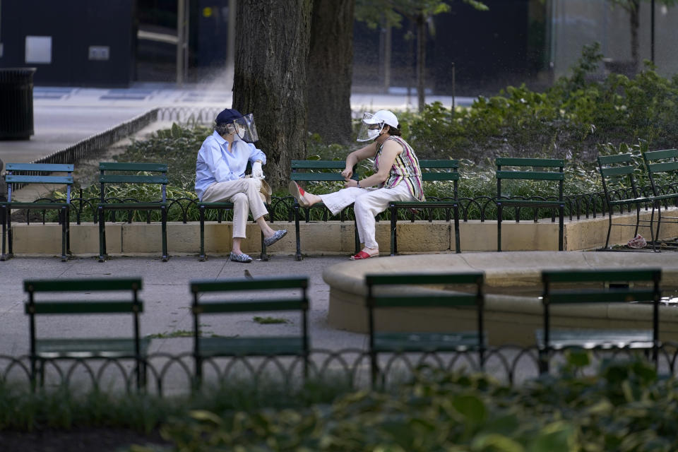 Two women wearing protective masks and face shields talk in a small park around the historic Water Tower on Chicago's Magnificent Mile on Tuesday, Aug. 11, 2019. (AP Photo/Charles Rex Arbogast)