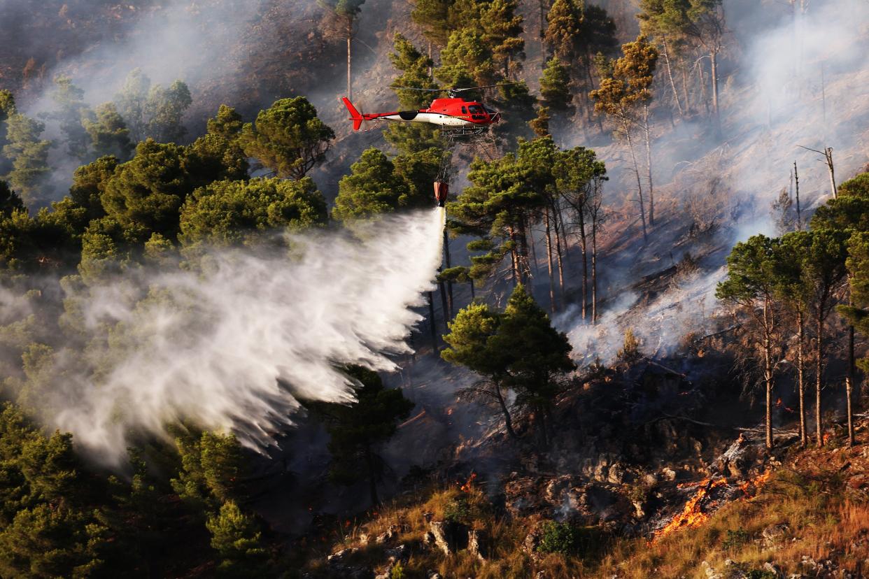 A firefighter helicopter drops water to intervene burning area during wildfire which continues to grow as it started the previous day in the scrub area in Palermo (Anadolu Agency via Getty Images)