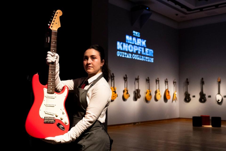 A Christie's art handler holds up Mark Knopfler's Red Schecter Telecaster guitar, among more than 120 guitars to be sold at auction last month (PA)