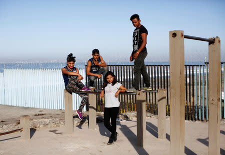 Anyi Loan Mejia (2nd R), 22, from Honduras and (L-R) Damaris Alejandra Tejeda, 15, Nelson Reniery Ruiz Maradiaga, and Jairo David Veliz, part of a caravan of thousands traveling from Central America en route to the United States, pose in front of the border wall between the U.S. and Mexico in Tijuana, Mexico, November 23, 2018. Loan Mejia said she dreamed of New York City's bright lights and skyscrapers, that she had seen in films. She said she believed "you can walk there without danger ... and that I could have things there I couldn't in Honduras, like a good job, wage and house, healthcare." REUTERS/Kim Kyung-Hoon