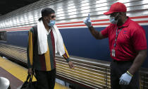 A traveler arriving on a train that originated in Miami gets directions from a porter, right, at Amtrak's Penn Station, Thursday, Aug. 6, 2020, in New York. Mayor Bill de Blasio is asking travelers from 34 states, including Florida where COVID-19 infection rates are high, to quarantine for 14 days after arriving in the city. (AP Photo/Mark Lennihan)