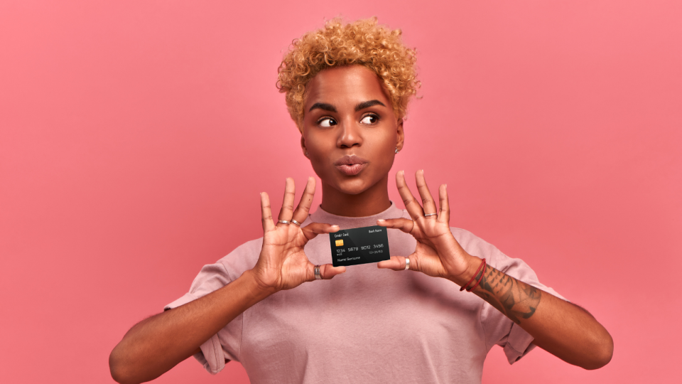 A woman holds a credit card on a pink background.