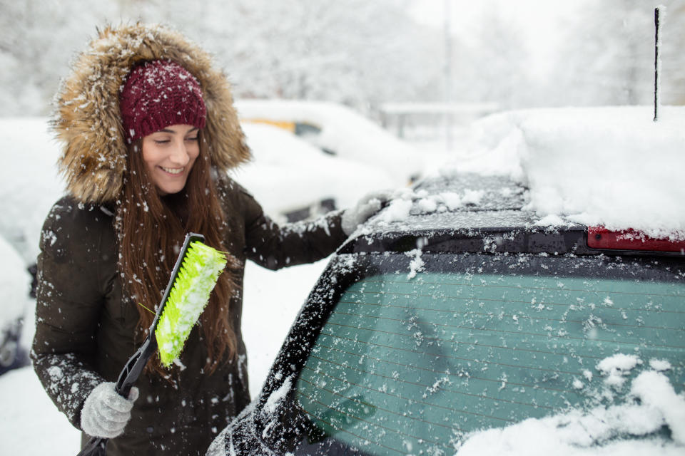 Young woman cleaning snow off her car