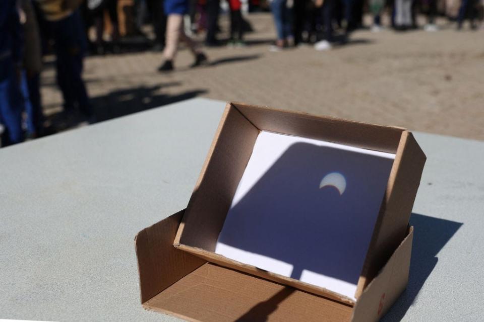 People observe a partial solar eclipse on a paper through a telescope in Ankara, on October 25, 2022.