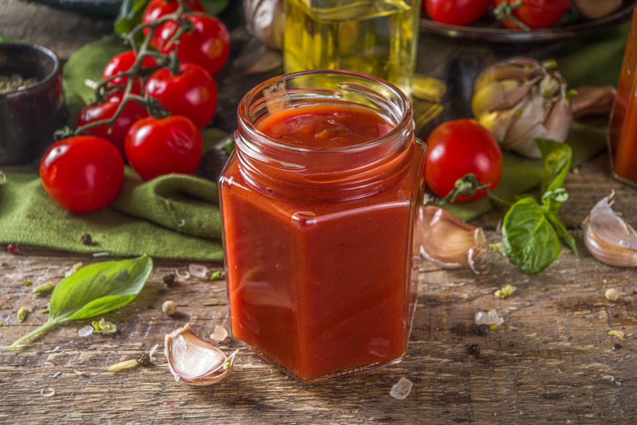 Homemade tomato sauce with basil, garlic and fresh tomatoes. Ketchup, marinara sauce in small jars. On a wooden background, with fresh vegetables and basil.