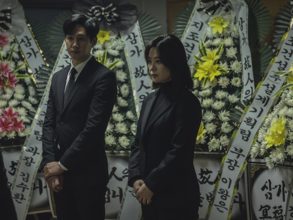 Yang Jae-seok and Yoon Seo-ha in the bequeathed, standing in black clothes in front of funeral bouquets