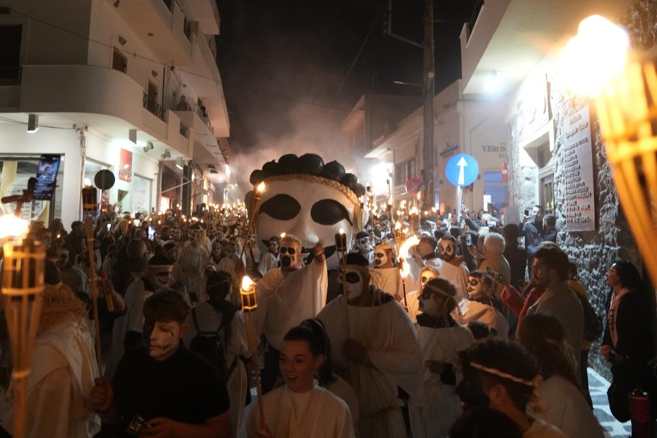 Young men and women with faces painted wear white sheets and hold torches on long poles, take part at the Torch Parade (Lampadiforia) on the Aegean Sea island of Naxos, Greece, late Saturday, Feb. 25, 2023. The first proper celebration of the Carnival after four years of COVID restrictions, has attracted throngs of revellers, Greek and foreign, with the young especially showing up in large numbers. (AP Photo/Thanassis Stavrakis)