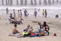 People sit on the beach Sunday, April 26, 2020, in Huntington Beach, Calif. A lingering heat wave lured people to California beaches, rivers and trails again Sunday, prompting warnings from officials that defiance of stay-at-home orders could reverse progress and bring the coronavirus surging back. (AP Photo/Marcio Jose Sanchez)