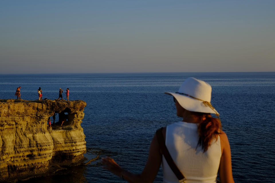 Tourists visit the sea caves during sunset at in southern coastal resort of Ayia Napa in southeast Mediterranean island of Cyprus, Sunday, May 29, 2022. Hundreds of Russian and Ukrainian Orthodox faithful visiting Cyprus would stream daily past the icon of the Virgin Mary at Kykkos Monastery to venerate the relic that tradition dictates was fashioned by Luke the Evangelist and blessed by the Virgin herself. But a European Union ban on flights to and from Russia as a result of Russia's invasion of Ukraine has meant a loss of 800,000 vacationers - a fifth of all tourists to Cyprus in record-setting 2019. (AP Photo/Petros Karadjias)