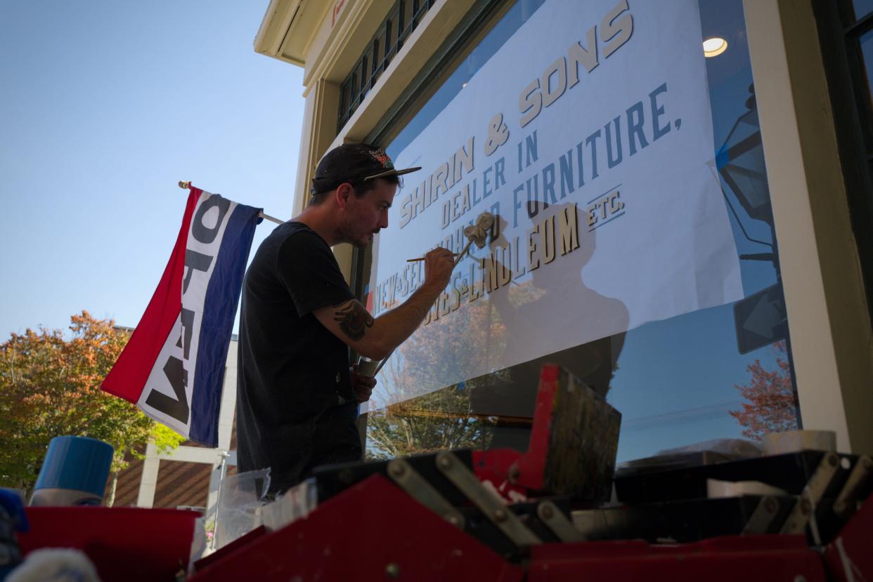 Movie set sign painter, Brian Denahy, paints the windows of The Drawing Room on William Street in New Bedford to resemble a 1930's furniture store for an AMC movie being filmed in New Bedford.